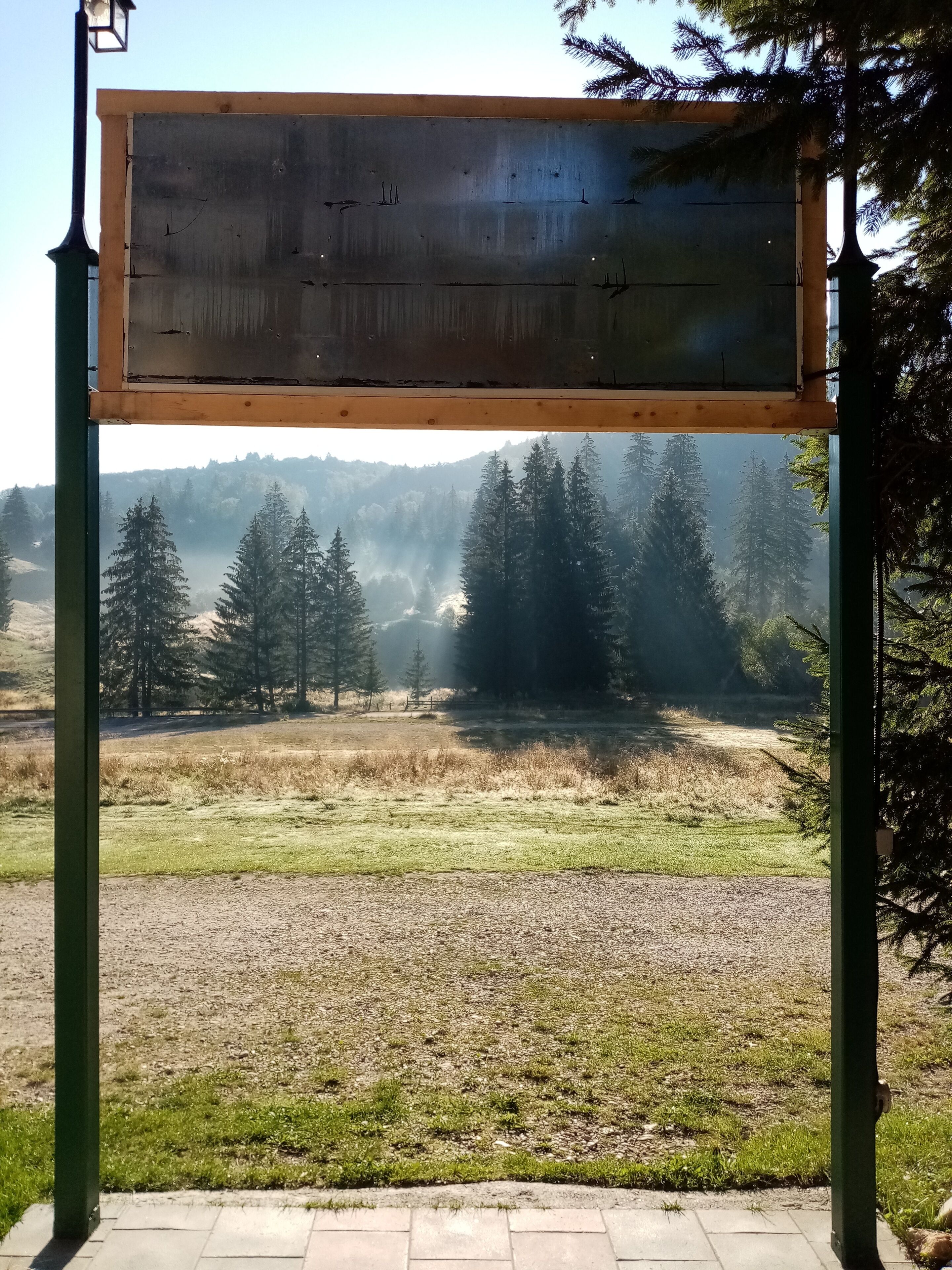 A wooden sign with a view of a forest and mountains in the background.