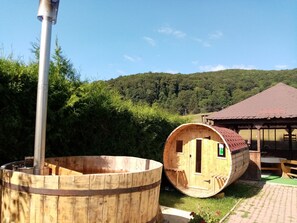 A wooden sauna structure with a chimney, a wooden barrel-shaped sauna, and a small wooden building with a tiled roof. - Pensiunea Poiana Cristian (Brasov)