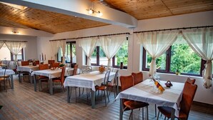 A dining area with tables set for four, wooden flooring, and large windows with curtains.