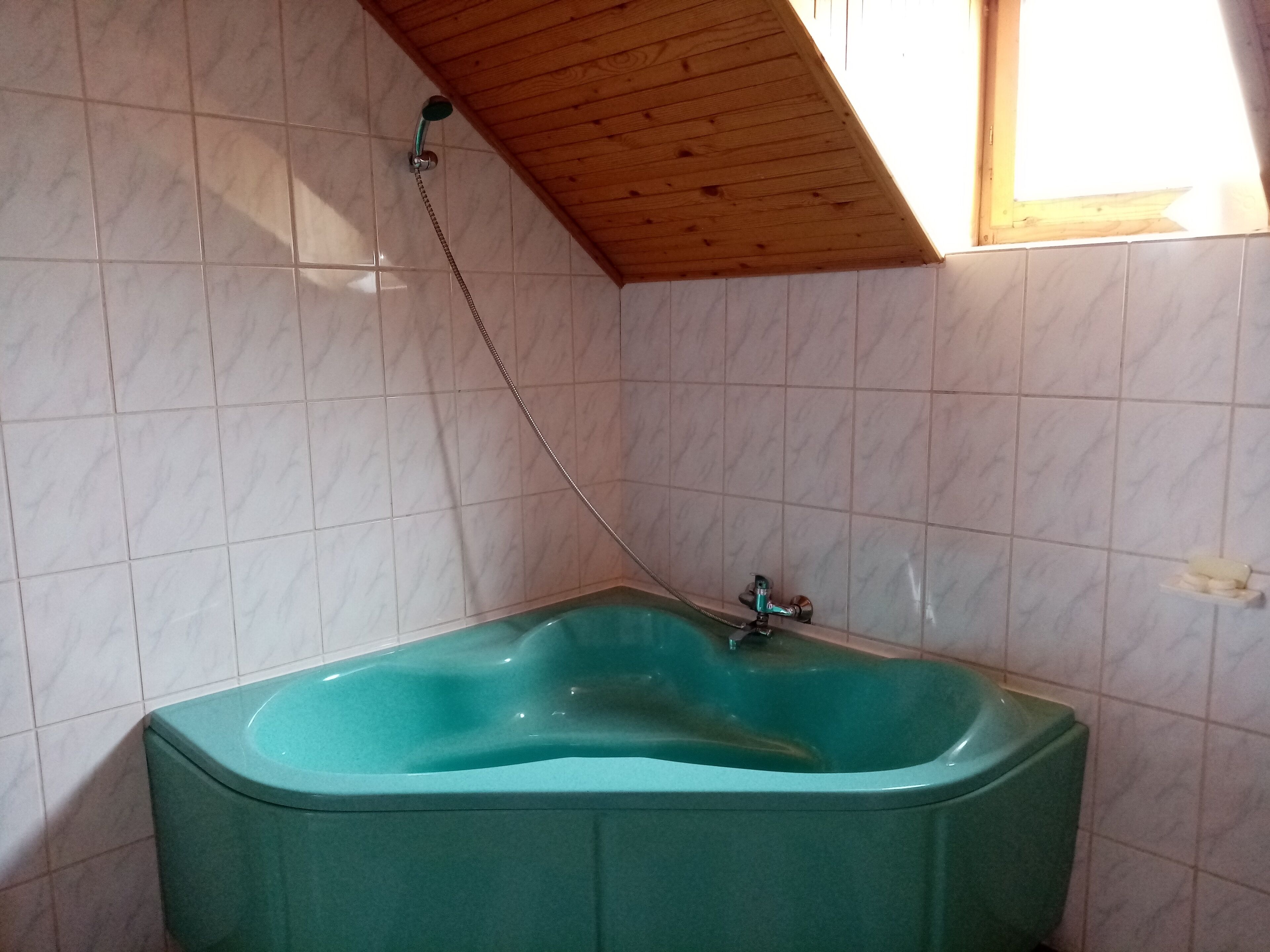 A bathroom with a freestanding bathtub, tiled walls, and a wooden ceiling.