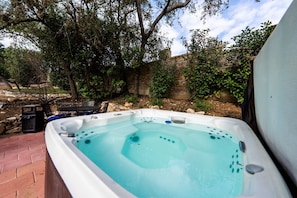 Un bain à remous dans un jardin, entouré d’arbres et bordé d’un mur en briques.