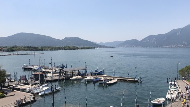 A marina with boats docked, a covered waiting area, and mountains in the background. - Iseo Lake View - the window on the harbor (Iseo)