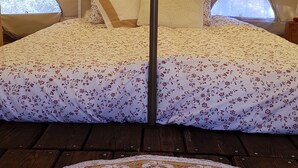 Una carpa con una cama, ropa de cama estampada con motivos florales, un tapete circular tejido y vistas a árboles a través de las ventanas de la carpa.