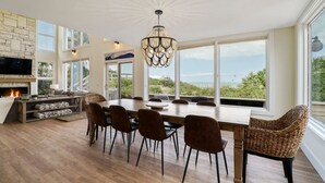 Tilava olohuone, jossa on suuri ruokapöytä, mukavat istuimet, takka ja näkymä ulos.