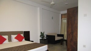 Una habitación de hotel con una cama grande, una silla, una mesita pequeña y una planta en maceta.