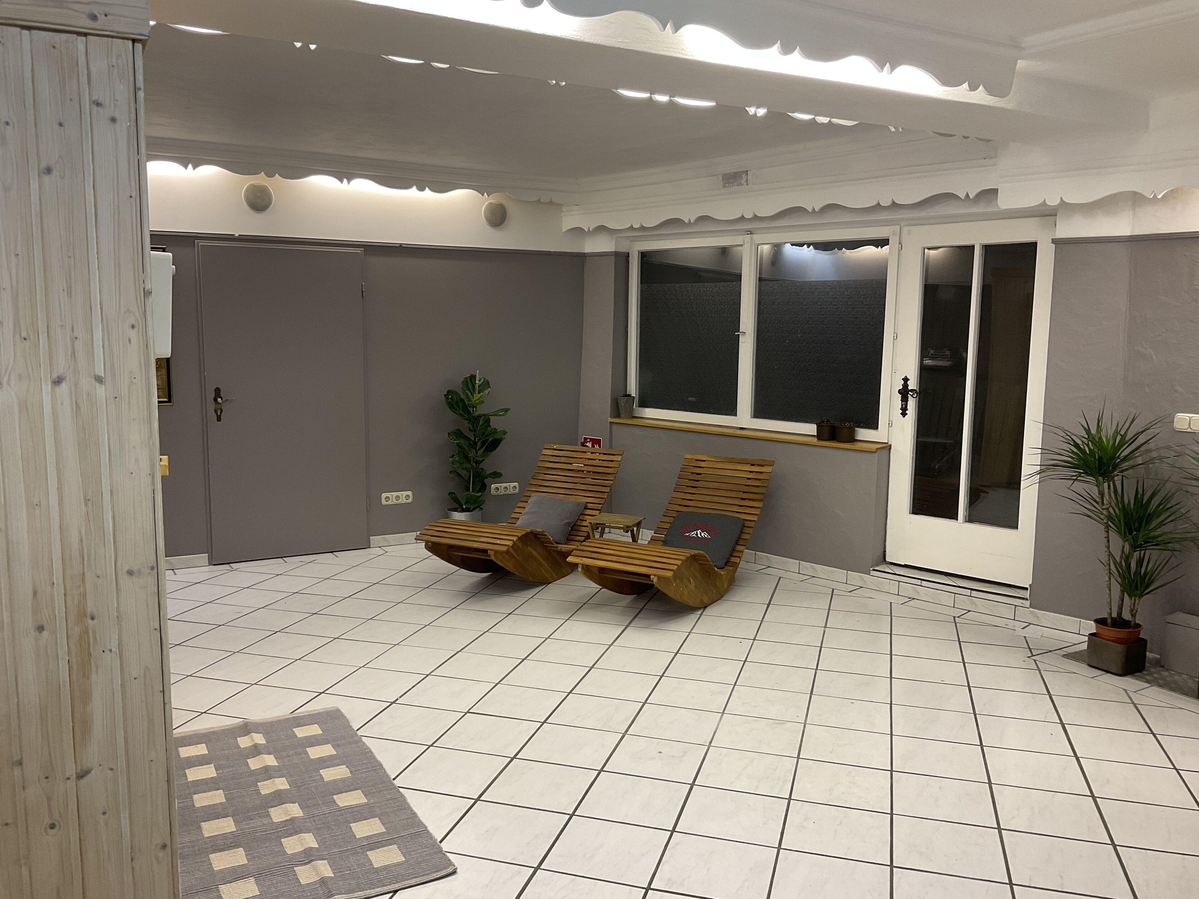 Ein Zimmer mit zwei Holz-Loungesesseln, einem Blumentopf und einem Fenster mit Blick.