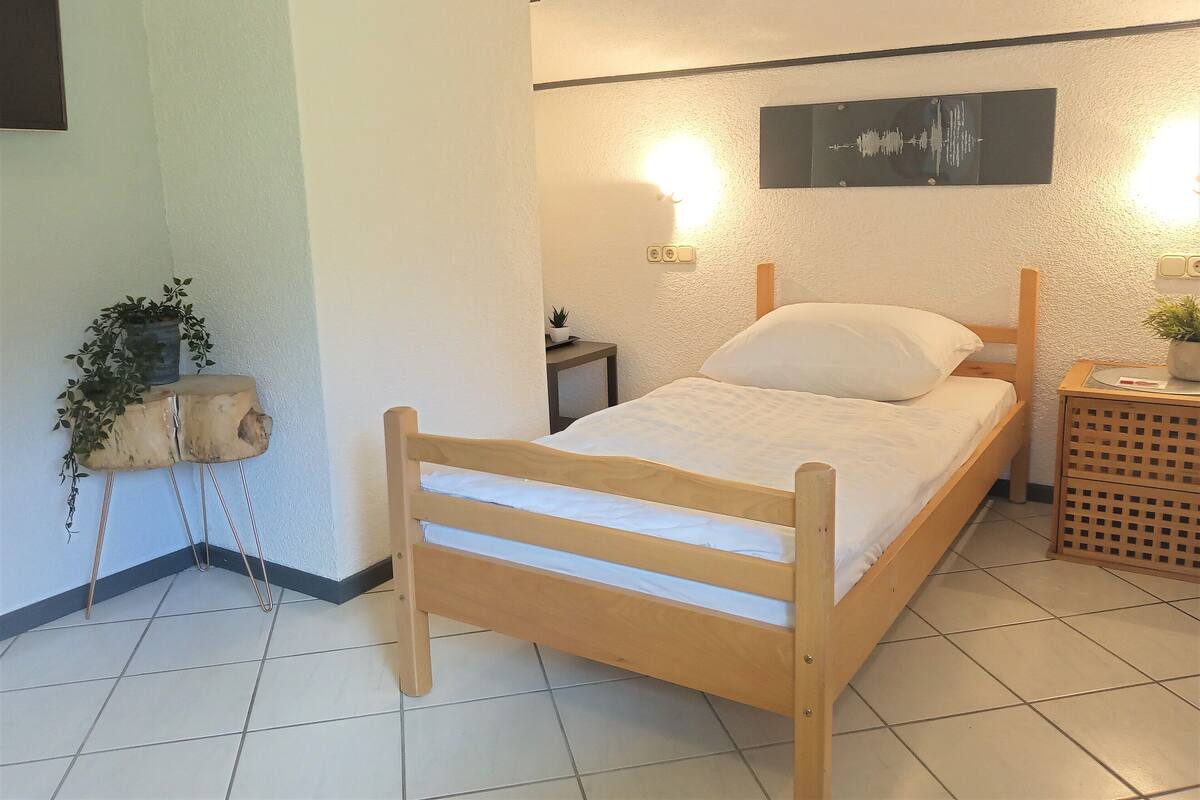Une chambre à coucher avec un lit en bois, une table de chevet, une étagère murale ornée de plantes et une horloge murale.
