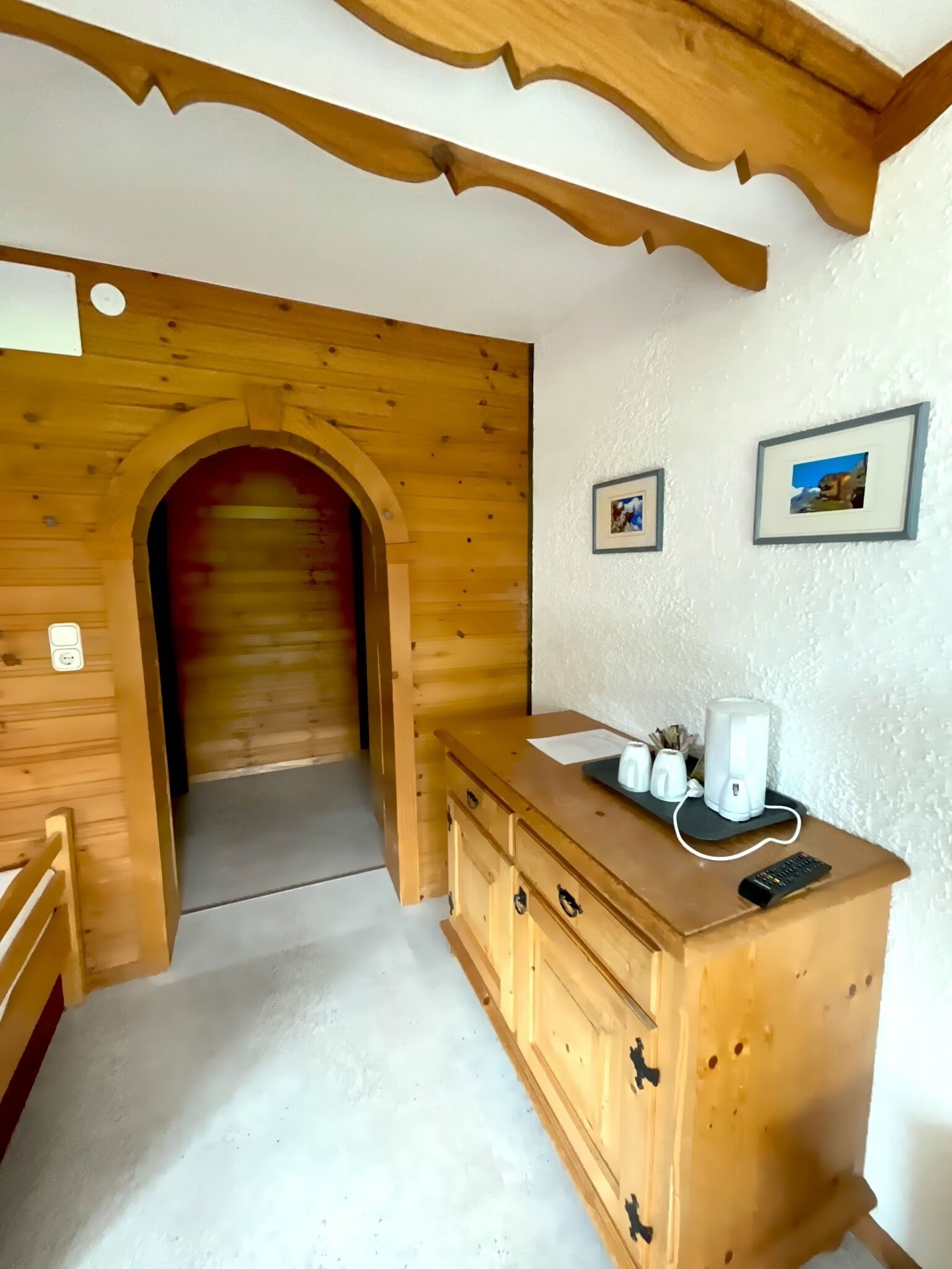 A wooden interior with a wooden bench, a wooden cabinet with drawers, and a white wall with two framed pictures.