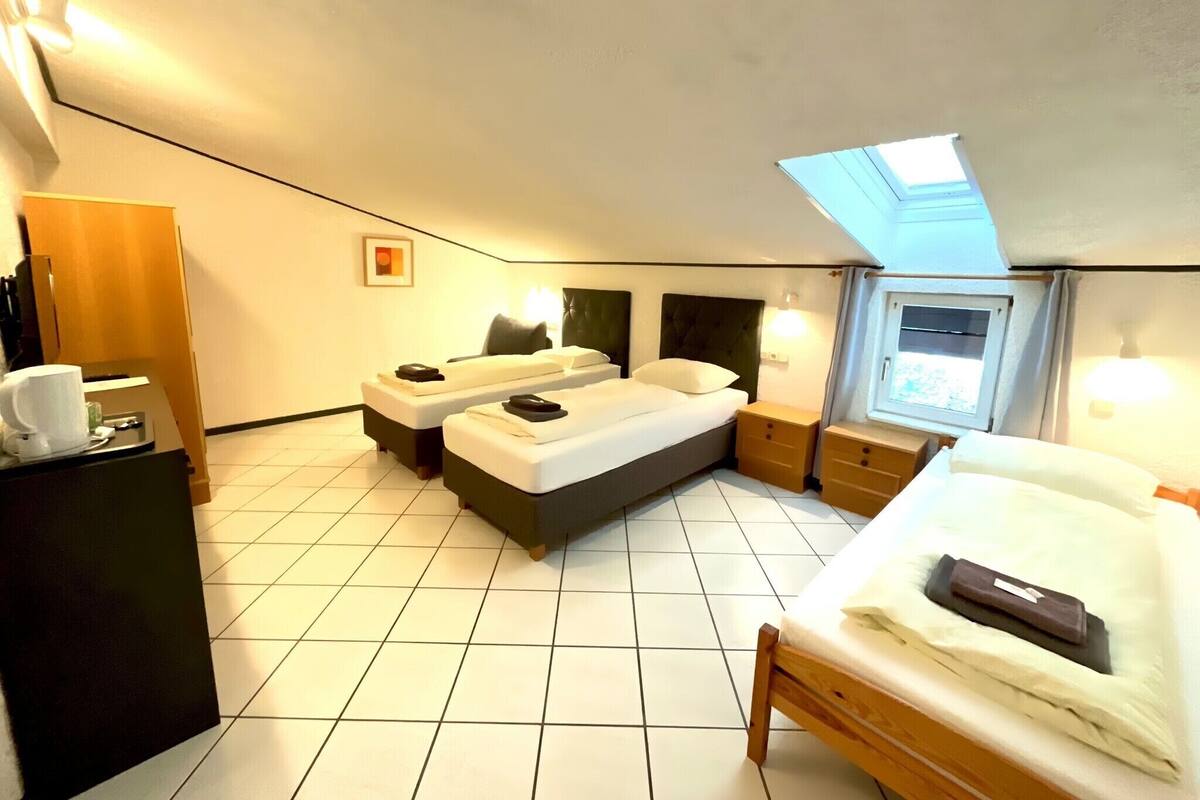 Une chambre d’hôtel de taille modeste, équipée de deux lits, d’un bureau et d’une petite fenêtre.