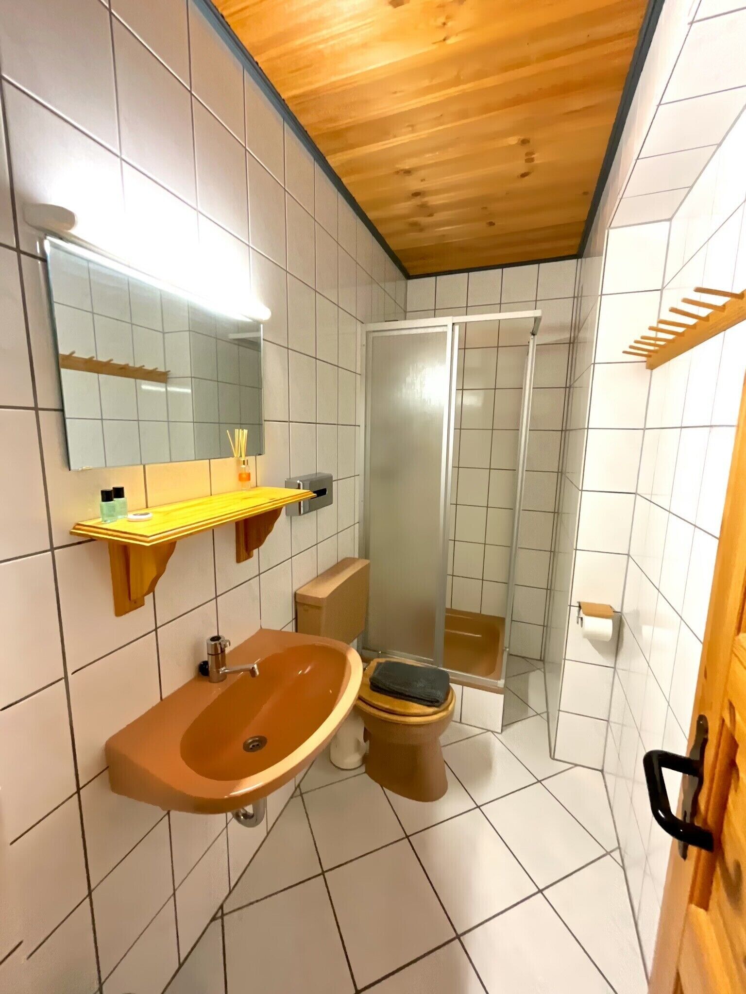 A bathroom with a wooden ceiling, white tiled walls, a wooden sink, a toilet, and a glass shower enclosure.
