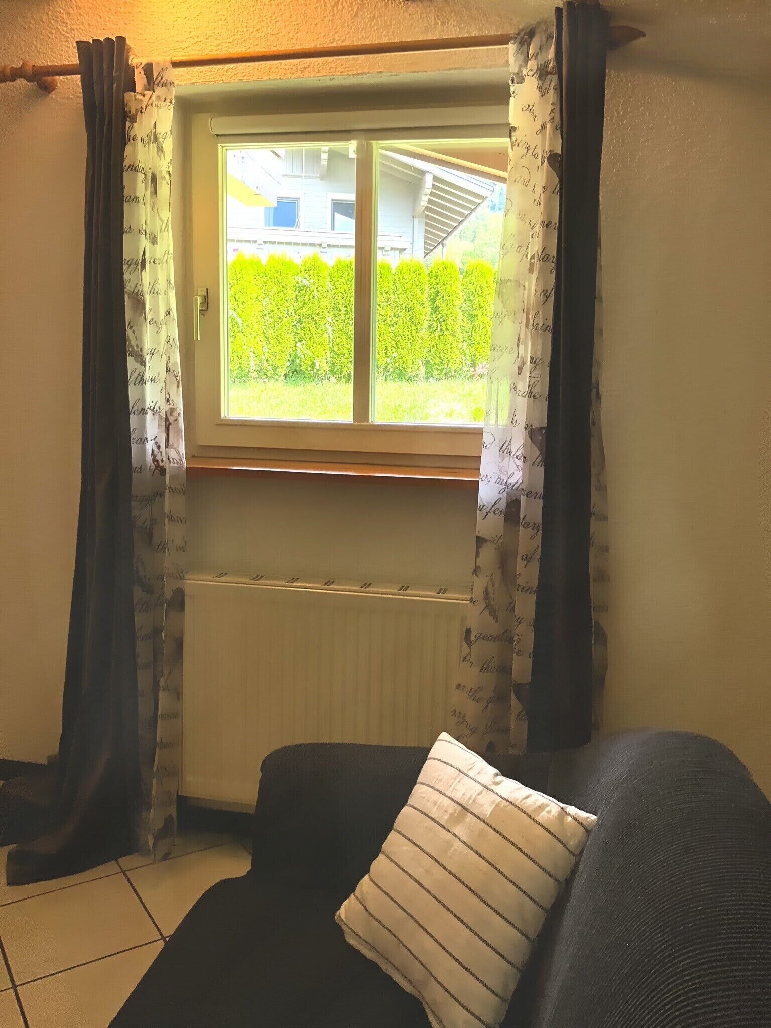 A room with a window, a radiator, and a black sofa with a striped pillow.