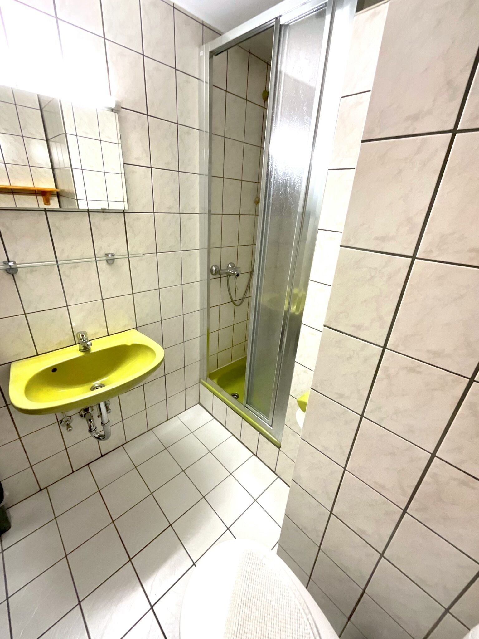 A bathroom with a yellow sink, a glass shower enclosure, and tiled walls.