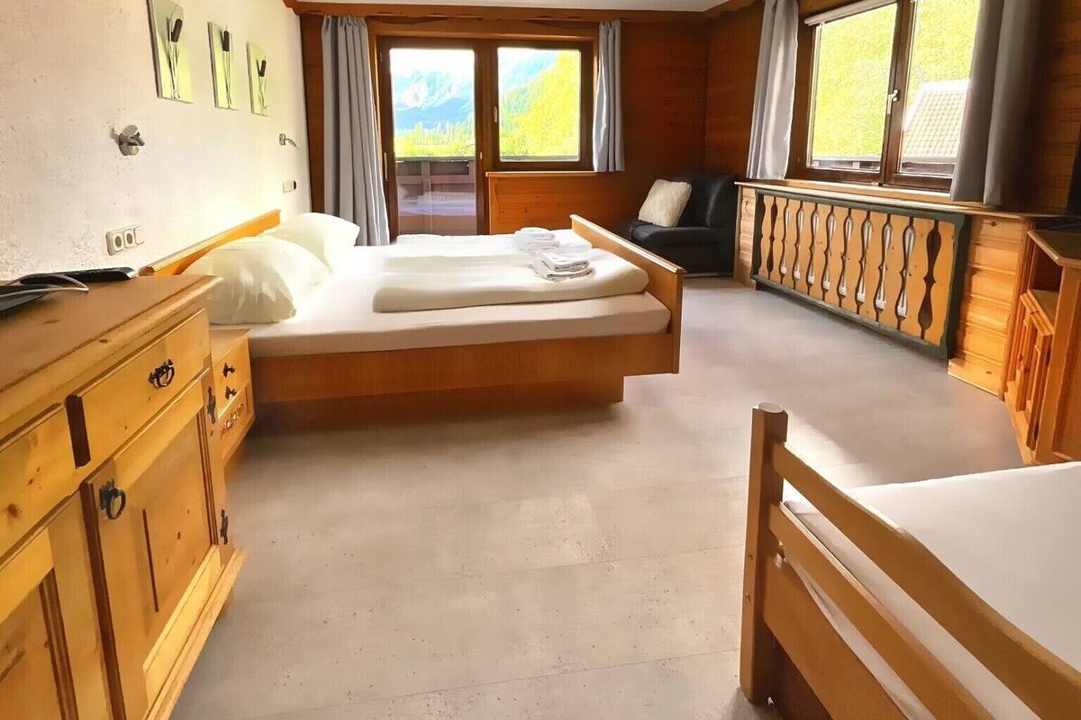 Une chambre avec un grand lit, une commode en bois et une vue sur l’extérieur par une fenêtre.