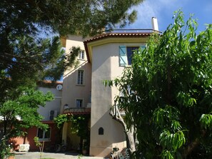 A two-story building with a beige facade, a red-tiled roof, and a balcony. There are windows with shutters, and a satellite dish is visible on the roof. - In the bird paradise, an oasis of silence, the best recreation for you! (Narbonne)