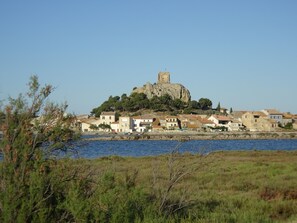A coastal town with a prominent castle-like structure on a hill, surrounded by residential buildings. - In the bird paradise, an oasis of silence, the best recreation for you! (Narbonne)