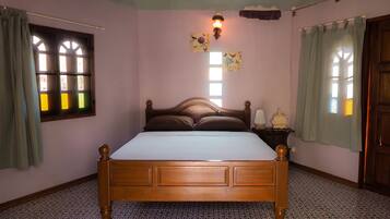 A bedroom with a wooden bed, a nightstand, a wall-mounted lamp, and a window with curtains.