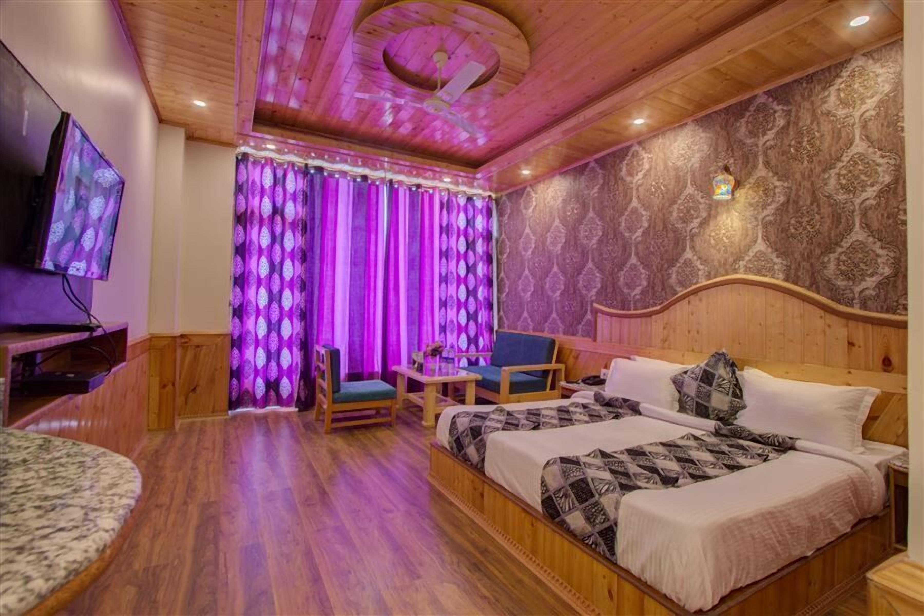 A wooden-floored room with a bed, two chairs, a small table, and a TV.