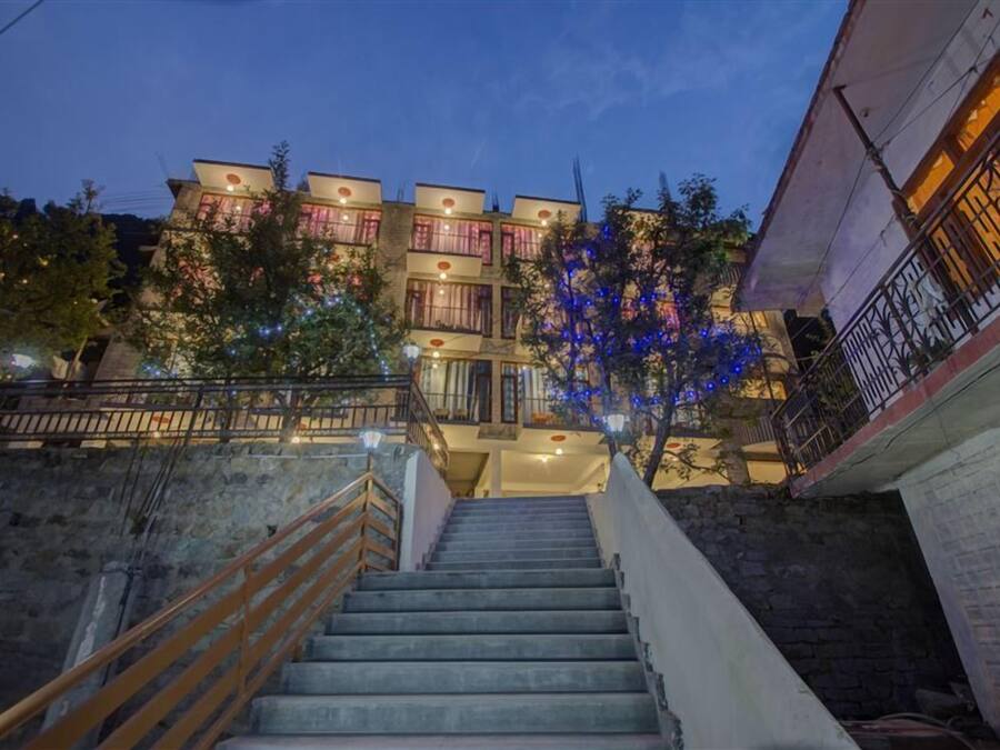 A multi-story building with a staircase leading to the entrance, surrounded by trees and illuminated by string lights.