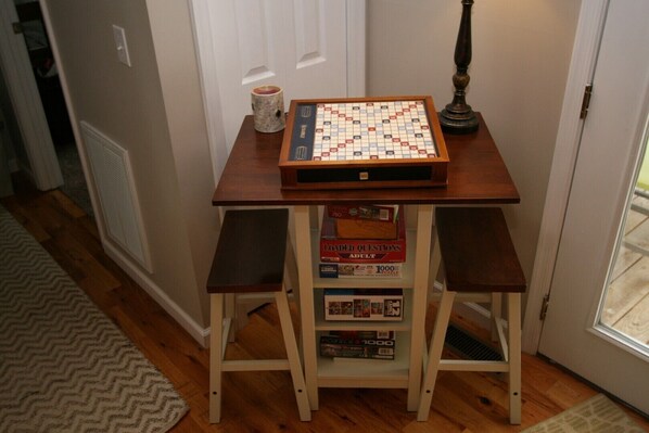 A table with a Scrabble board game, a candle, and a lamp.