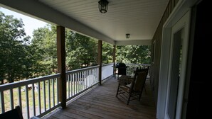 Une véranda couverte avec un plancher en bois, une balustrade blanche et une table entourée de chaises.