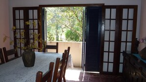 A dining area with a table set for four, a vase with yellow flowers, and a view of greenery through a sliding door.