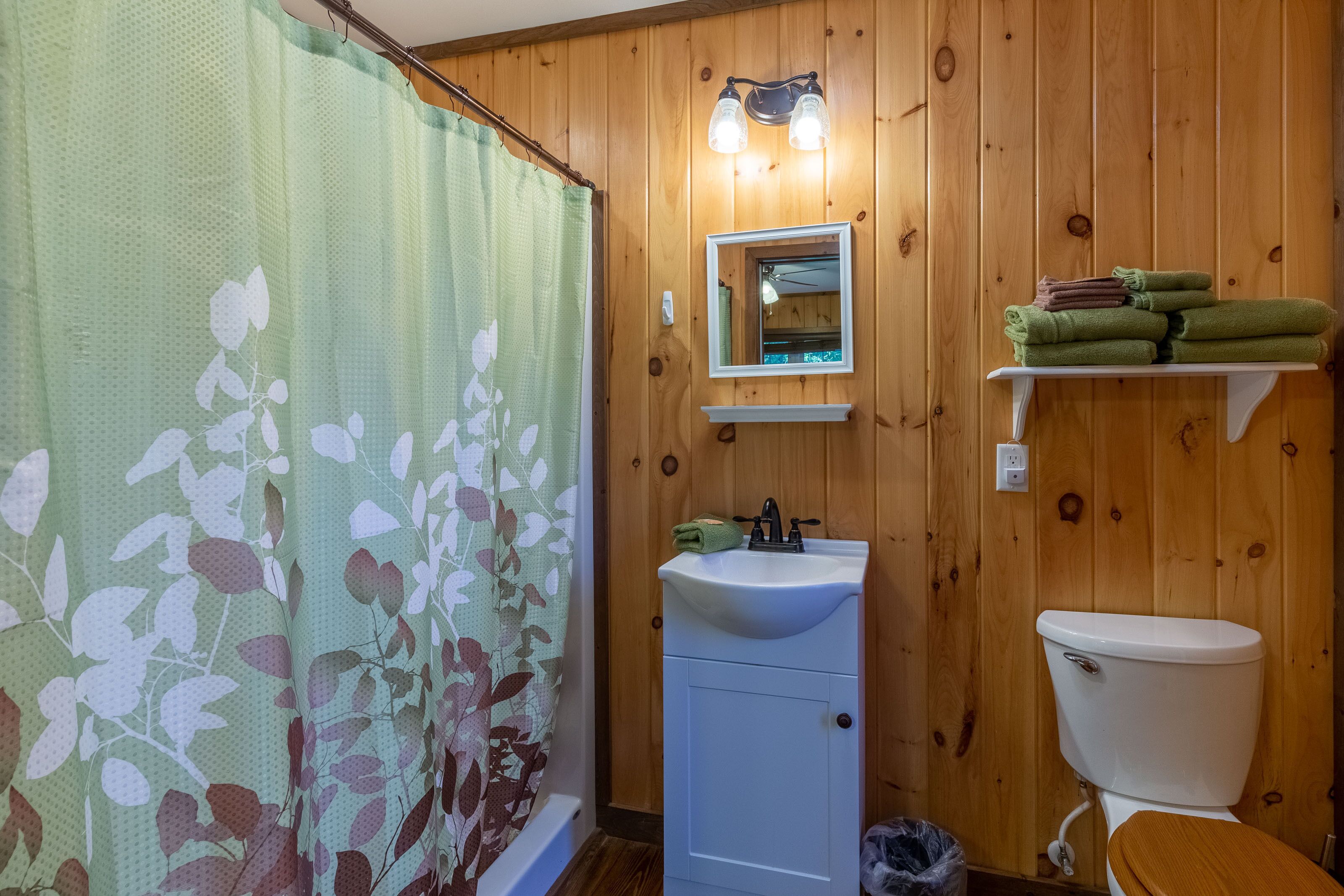 Un baño con paredes de madera, un lavamanos blanco, un espejo y un inodoro.