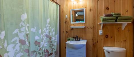 Un baño con paredes de madera, un lavamanos blanco, un espejo y un inodoro.