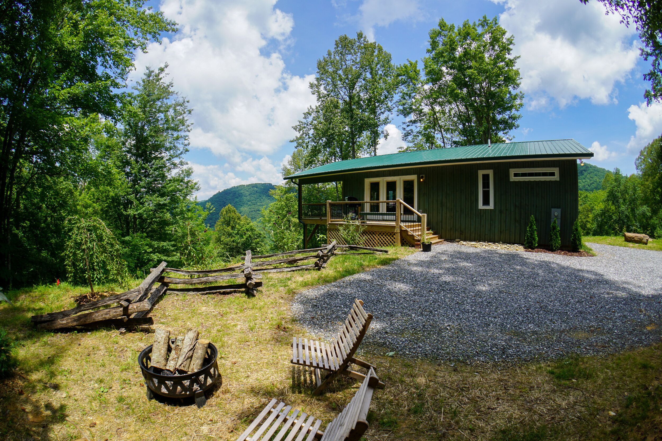 A rustic cabin with a green roof, a porch, and a gravel driveway.
