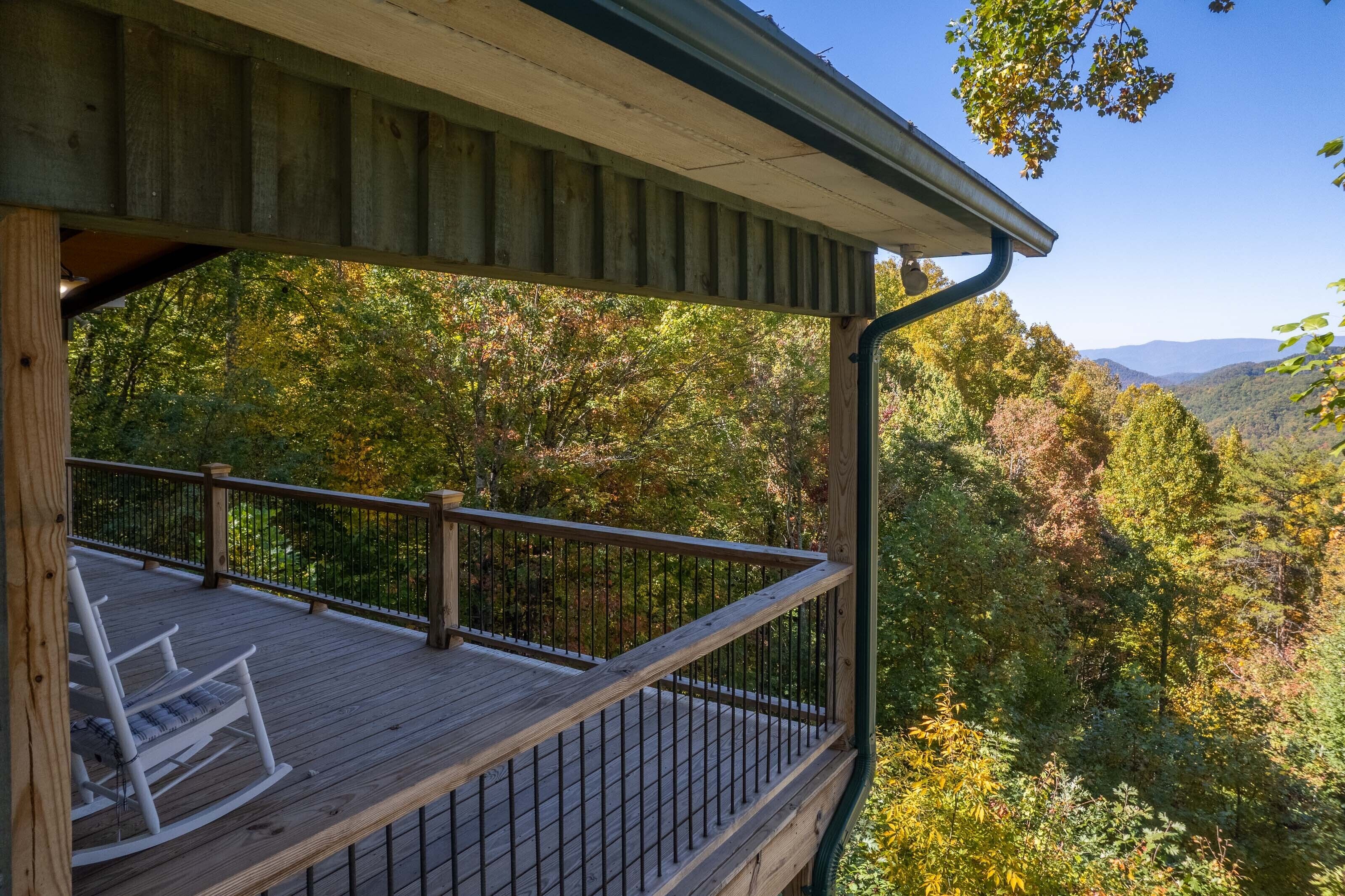 A wooden deck with a railing overlooking a forested area with mountains in the distance.
