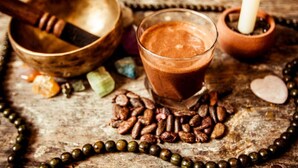 Una mesa de madera con un vaso de bebida de chocolate, un cuenco y una vela.