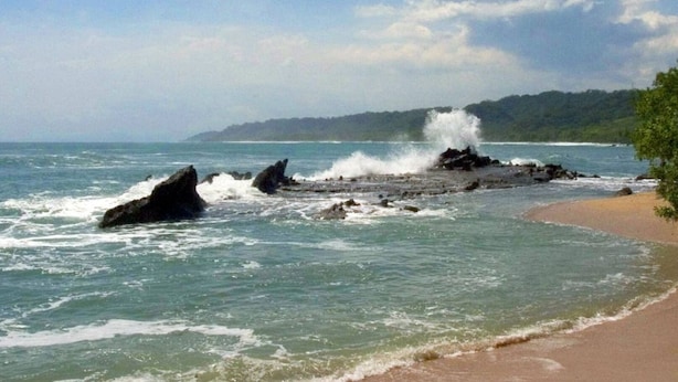 Una playa con afloramientos rocosos y olas rompiendo en la orilla.