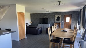 A modern living space with a dining area, a sofa, a TV, and a kitchen area. - Quiet setting with secure gated parking, children's play area & farm animals (upwell)