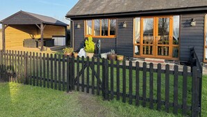 A two-story house with a dark exterior, large windows, and a wooden deck. - Quiet setting with secure gated parking, children's play area & farm animals (upwell)