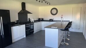 A modern kitchen with a central island, black appliances, white cabinetry, and a clock on the wall. - Quiet setting with secure gated parking, children's play area & farm animals (upwell)