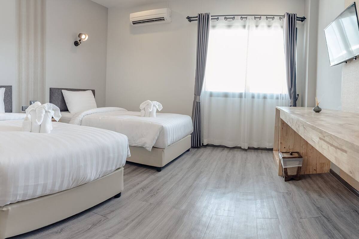Quarto de hotel com duas camas, uma escrivaninha de madeira, um espelho e uma televisão.