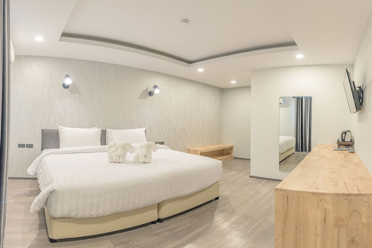 Um quarto moderno com cama curva, mesas de cabeceira, um banco de madeira e um espelho na parede.