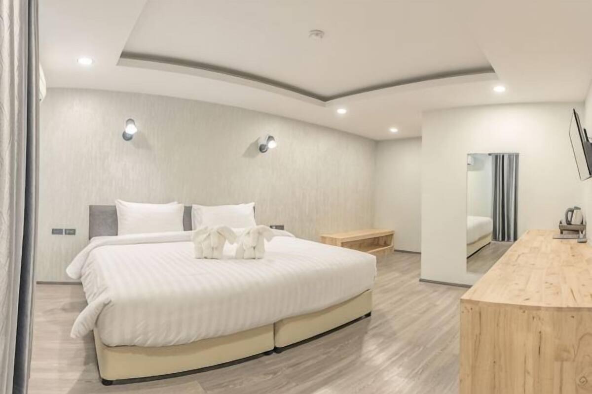 Quarto moderno com uma cama grande, mesas de cabeceira, uma escrivaninha de madeira e um espelho.