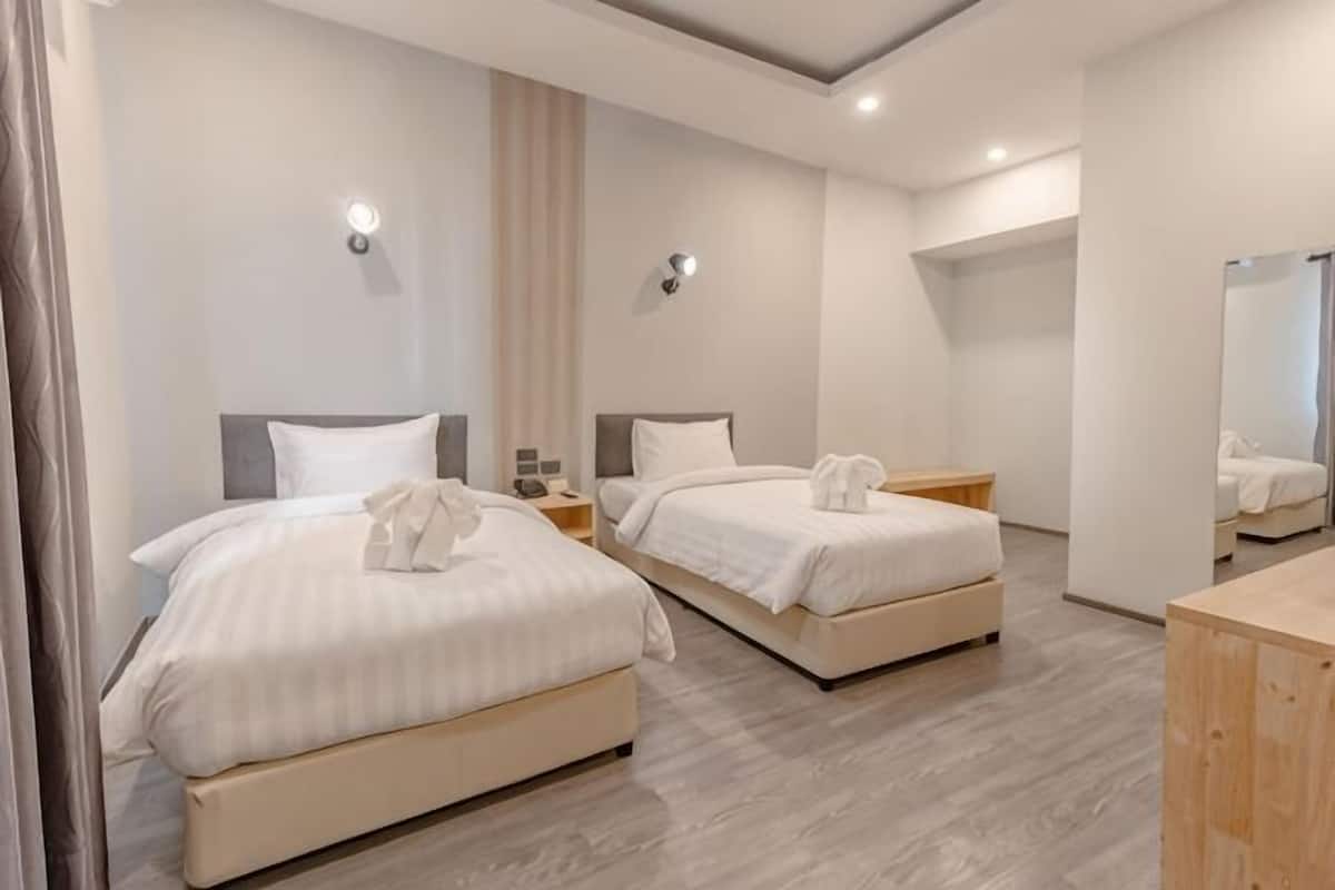 Quarto de hotel com duas camas, cômoda de madeira, espelho e banheiro ao fundo.