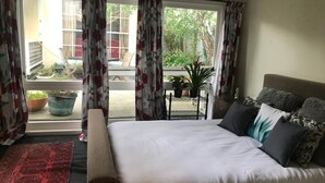 Un dormitorio con una cama, una mesita con plantas y vistas a un balcón con macetas.