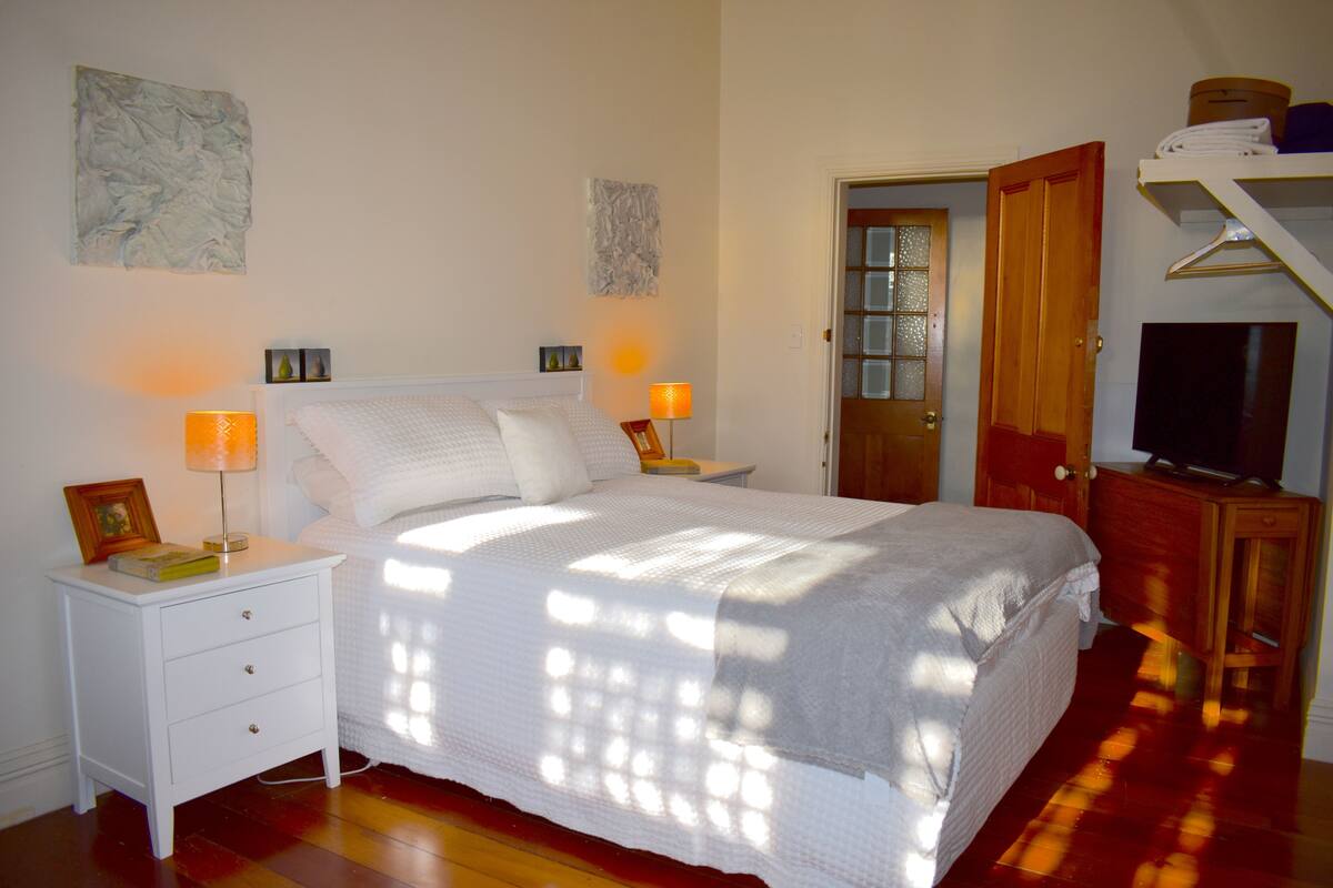 Un dormitorio con cama, mesitas de noche, cómoda, televisor y obras de arte en las paredes.