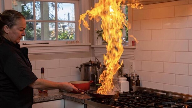 Una cocina con estufa a gas, una olla sobre la hornilla y llamas que suben del recipiente.