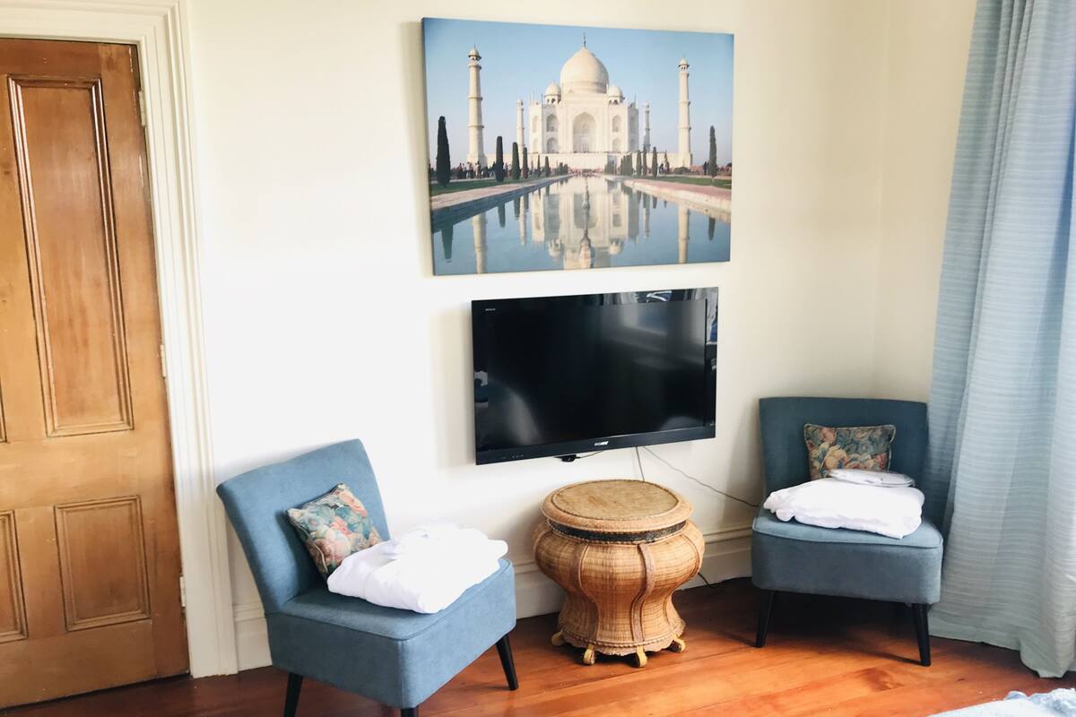 Una habitación con dos sillones azules, una mesa redonda de madera, un televisor de pantalla plana y un cuadro del Taj Mahal.
