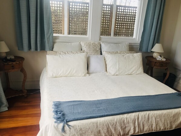 A neatly made bed with a blue throw blanket, two bedside tables with lamps, and a window with a wooden lattice. - Prodigal Daughter Gourmet Lodge (Martinborough)