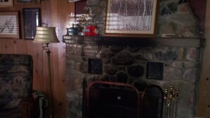 Ein gemütliches Wohnzimmer mit Kamin aus Stein, Holzwänden und einer bequemen Couch mit einer Decke.