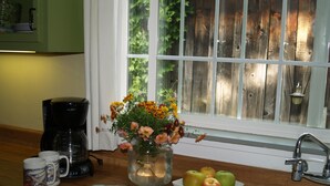 Eine Küchenarbeitsplatte mit Kaffeemaschine, Blumen in einer Vase, einer Schüssel Äpfel und zwei Tassen.