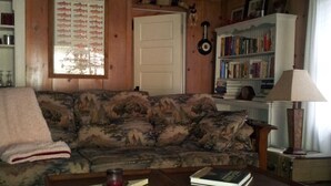 Ein gemütliches Wohnzimmer mit Holzboden, einem gemusterten Sofa, einem Couchtisch, einem Bücherregal und einer Tür.