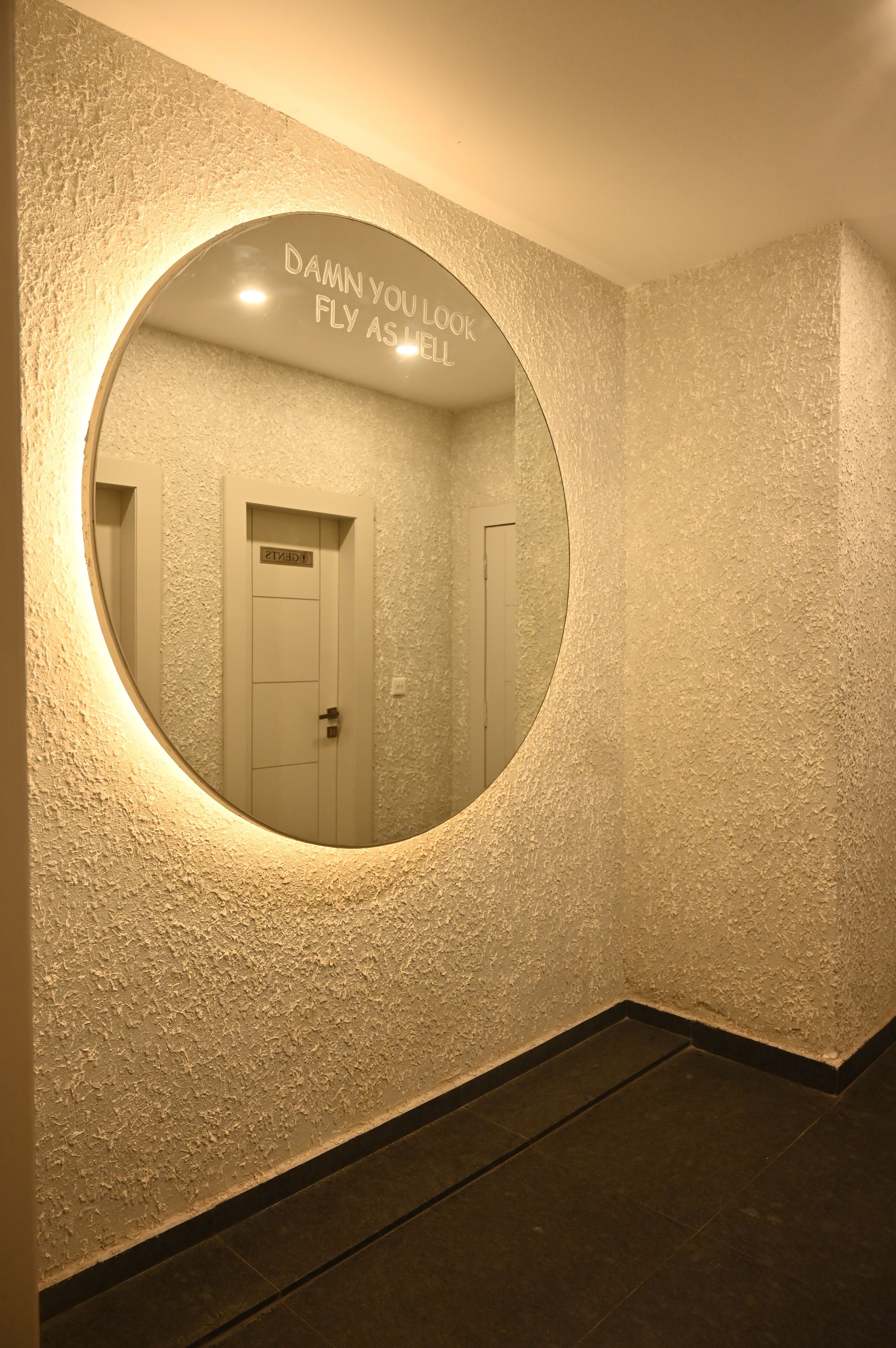 A circular mirror with a wall-mounted light, reflecting a door labeled "ZIOX".