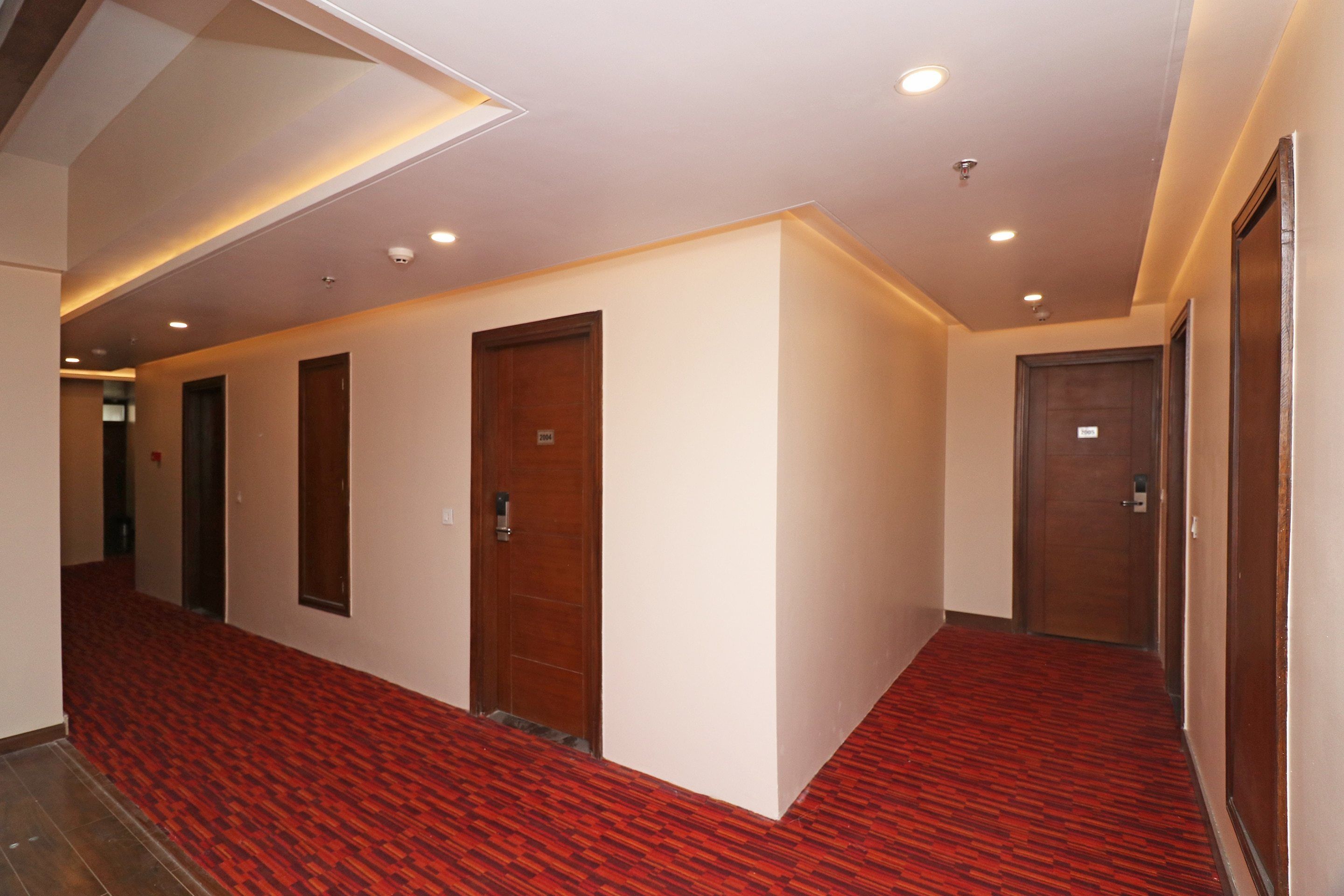 A hotel hallway with red patterned carpet, wooden doors, and recessed lighting.