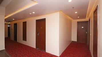 A hotel hallway with red patterned carpet, wooden doors, and recessed lighting.