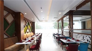 A restaurant with a long counter, red and blue chairs, and a green cushioned bench. - Hotel Vikram Palace (Varanasi)